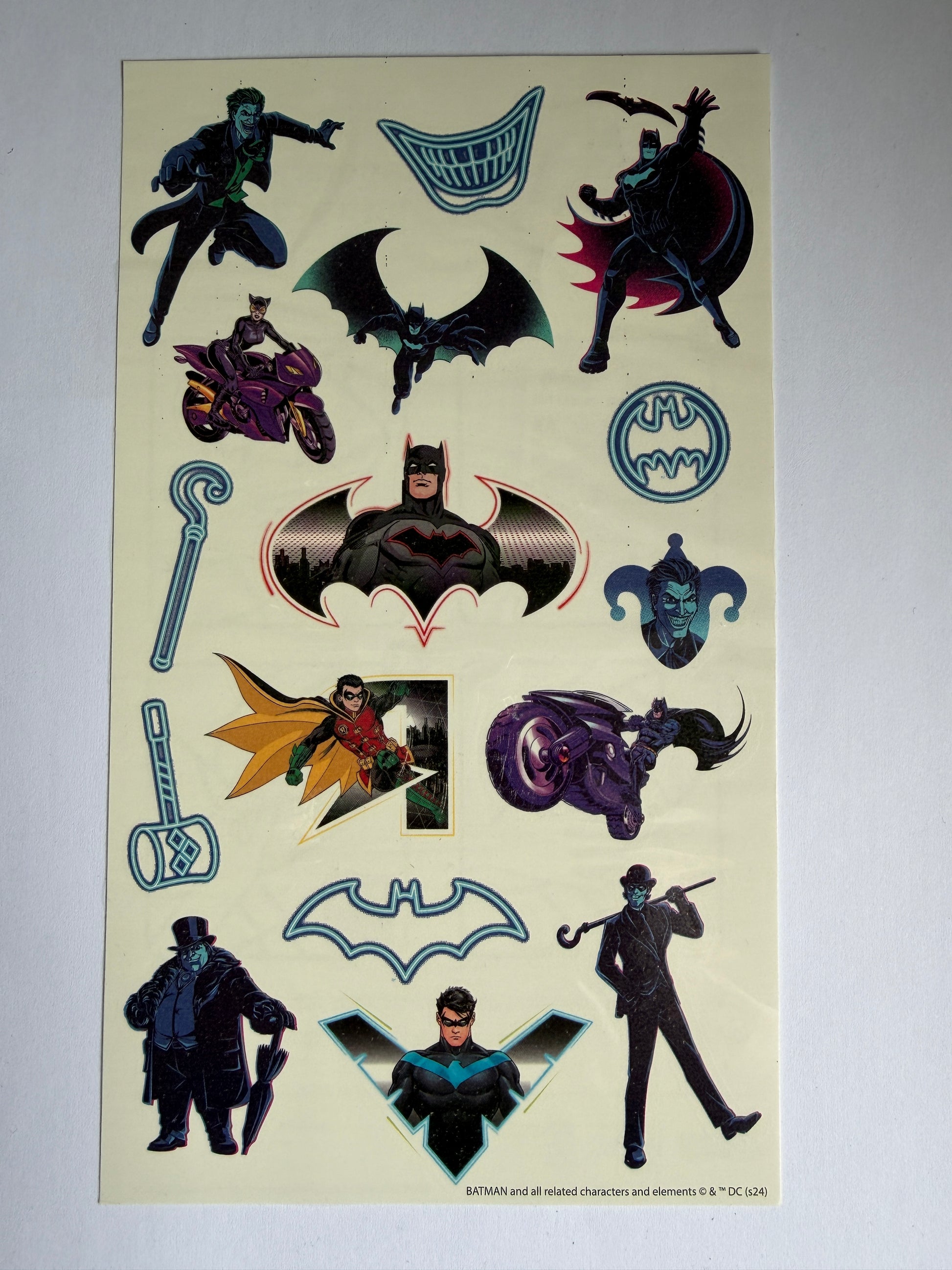 Sheet of superhero-themed stickers with various characters and symbols on a beige background.