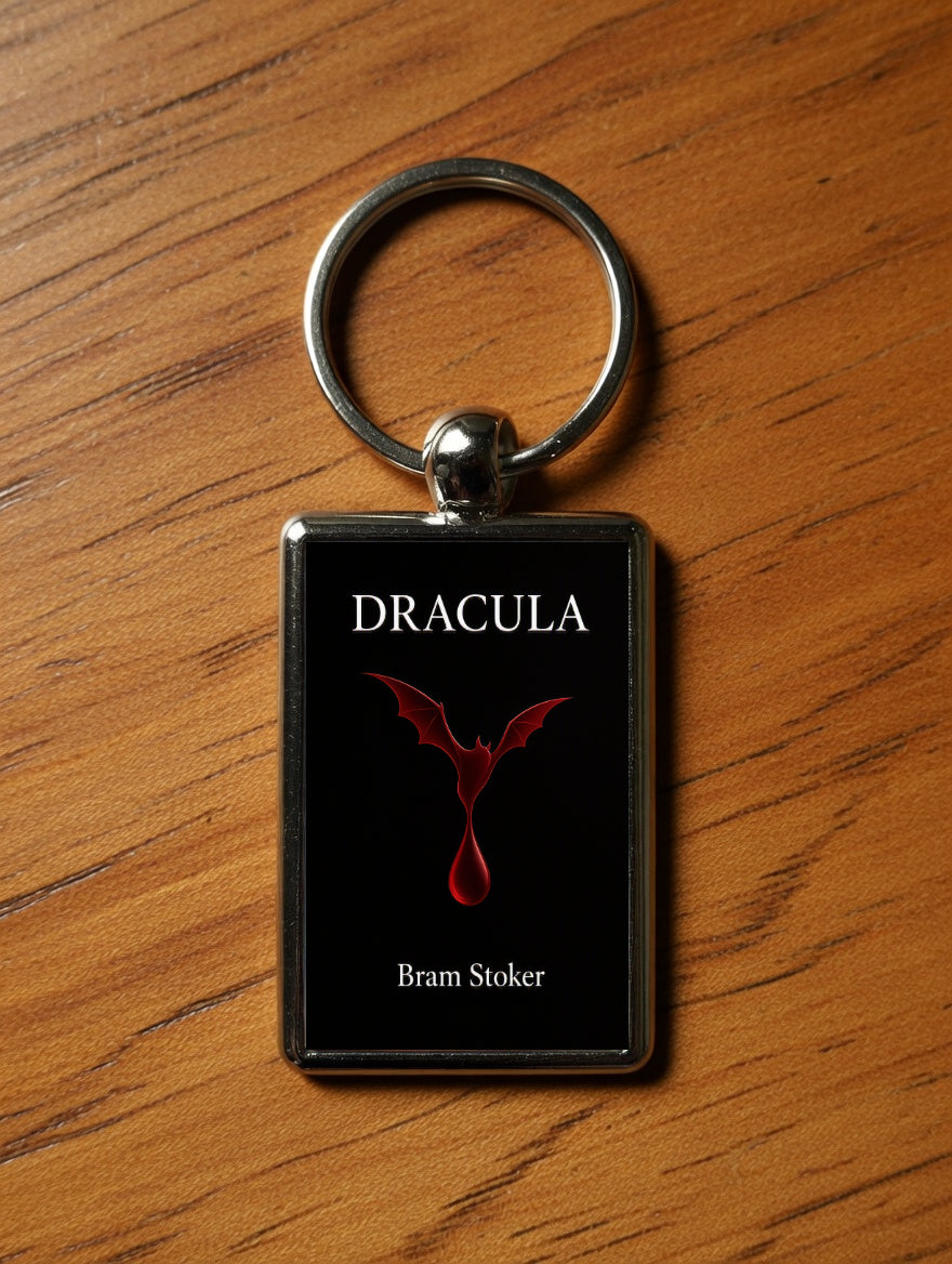 A rectangular keychain with a black face featuring the word 'DRACULA' in white, a red dragon emblem, and 'Bram Stoker' in white, attached to a silver metal ring and placed on a wooden surface.