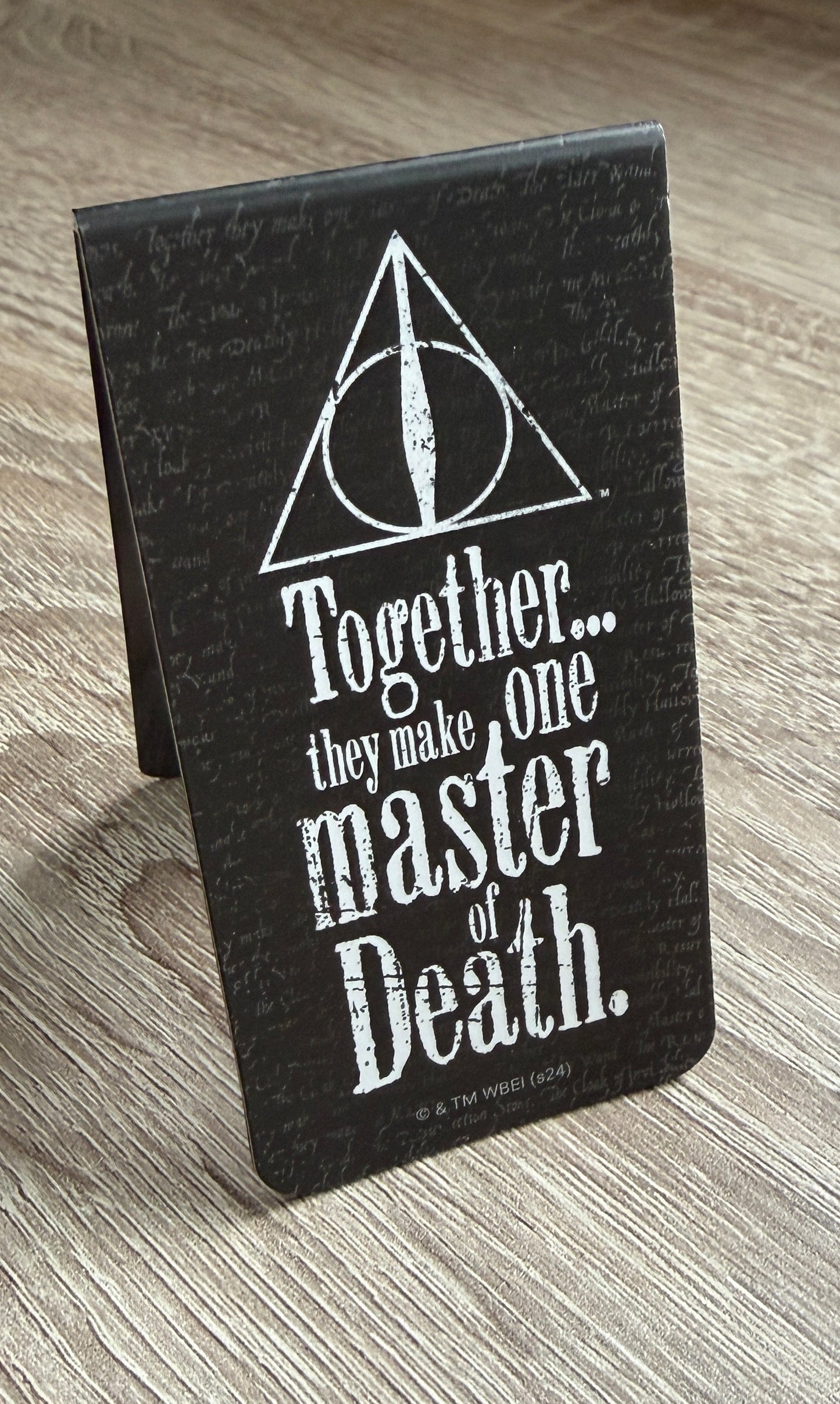Deathly Hallows Bookmark with white text and symbol on a wooden surface